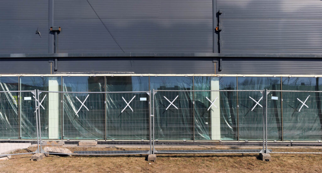 A steel fence encloses a construction site. Renovation of the old shopping center is being carried out. Panoramic collage from several outdoor photos